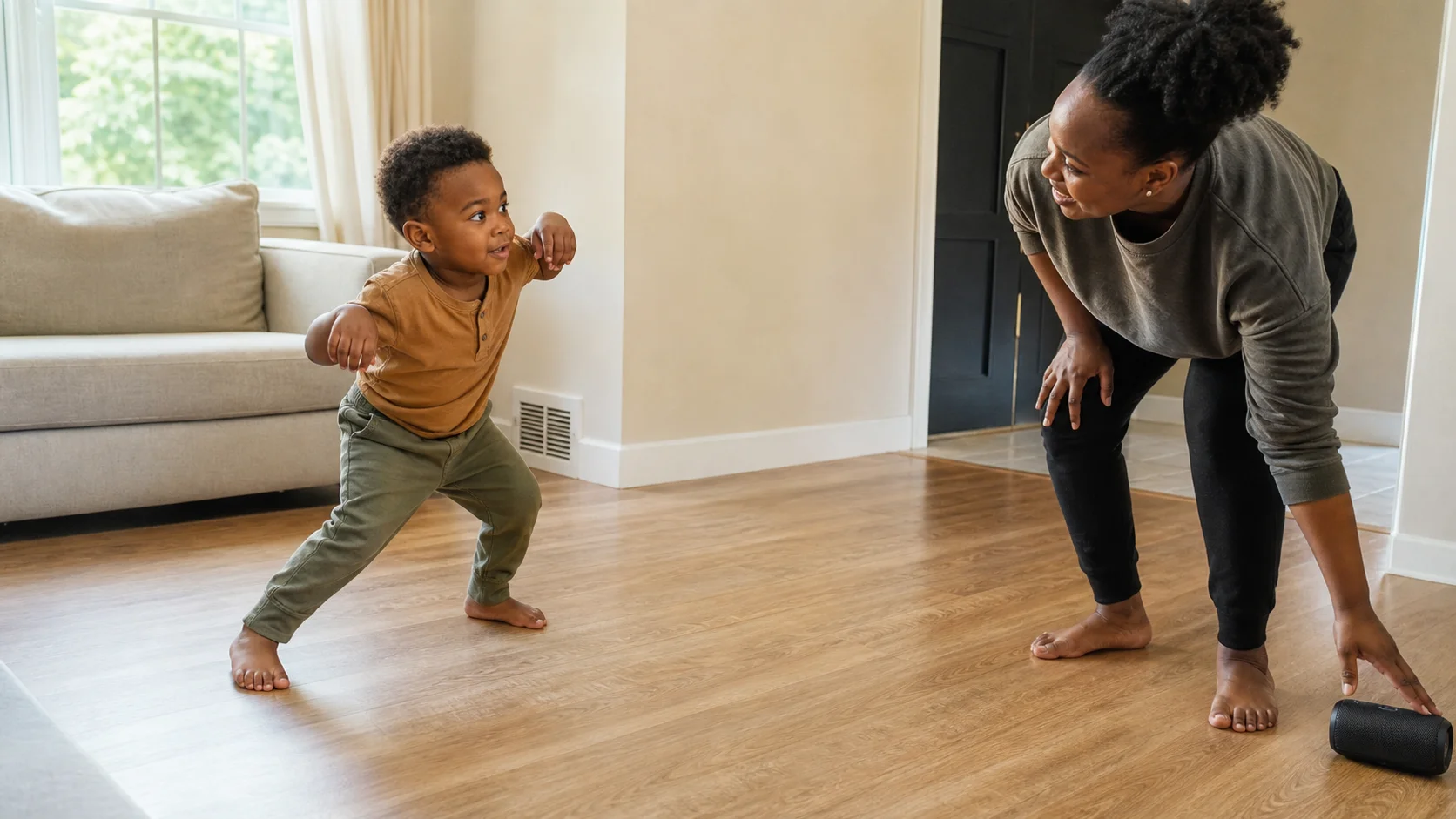 A toddler in an open indoor floor space moving like a tiger while a grown-up reaches toward a music player to stop the song.