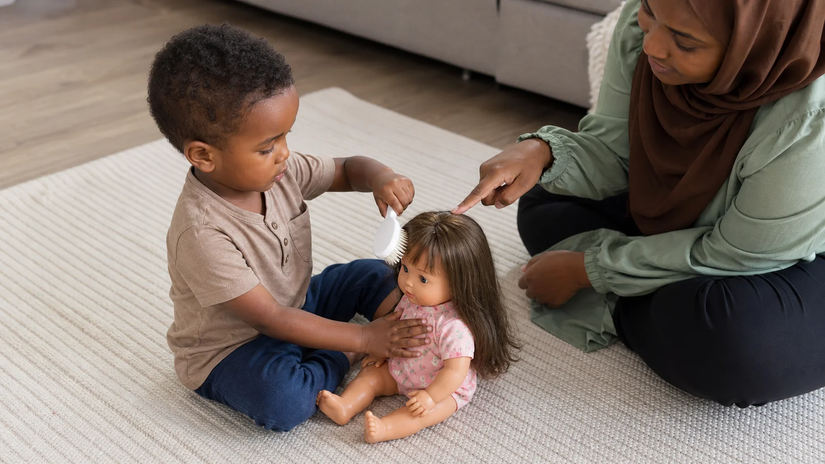 A toddler sitting with a grown-up and brushing a baby doll's hair with a soft brush.