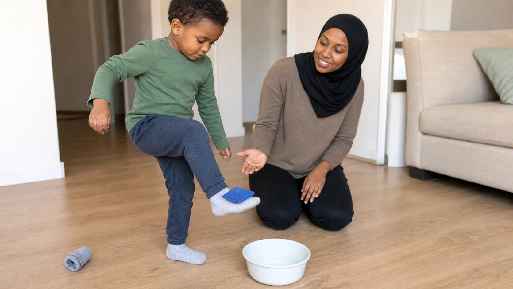Child slowly lifting one foot with a soft beanbag toward a close bucket target while a grown-up stays nearby