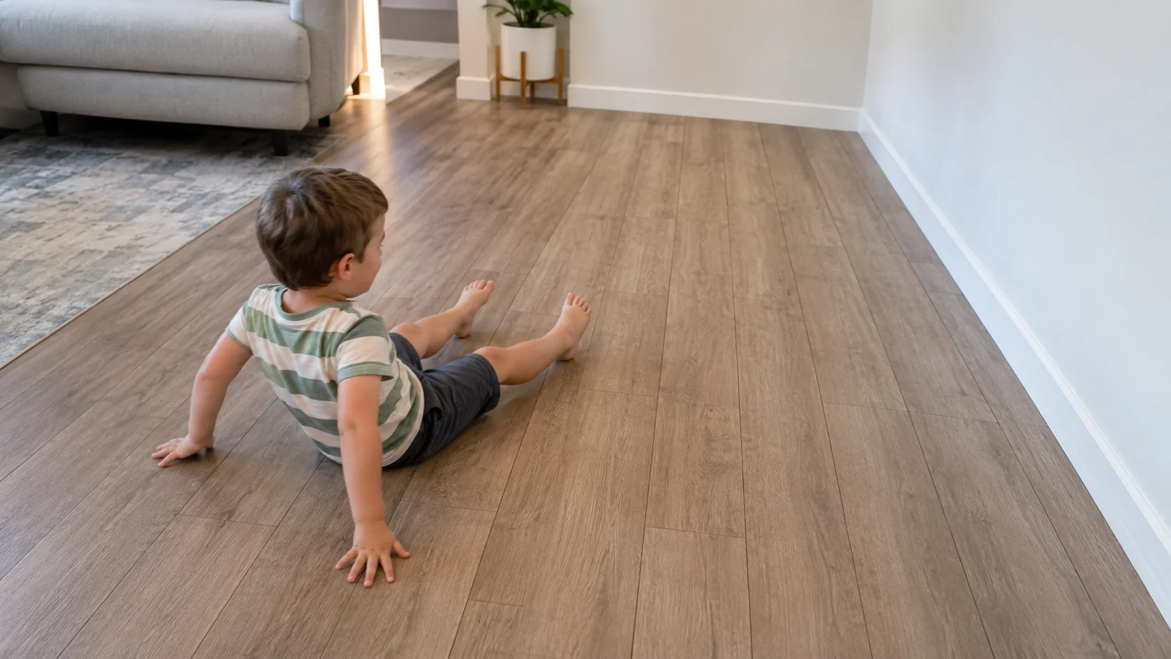 A young child sitting on the floor and scooting side to side toward a wall while a grown-up watches from nearby.