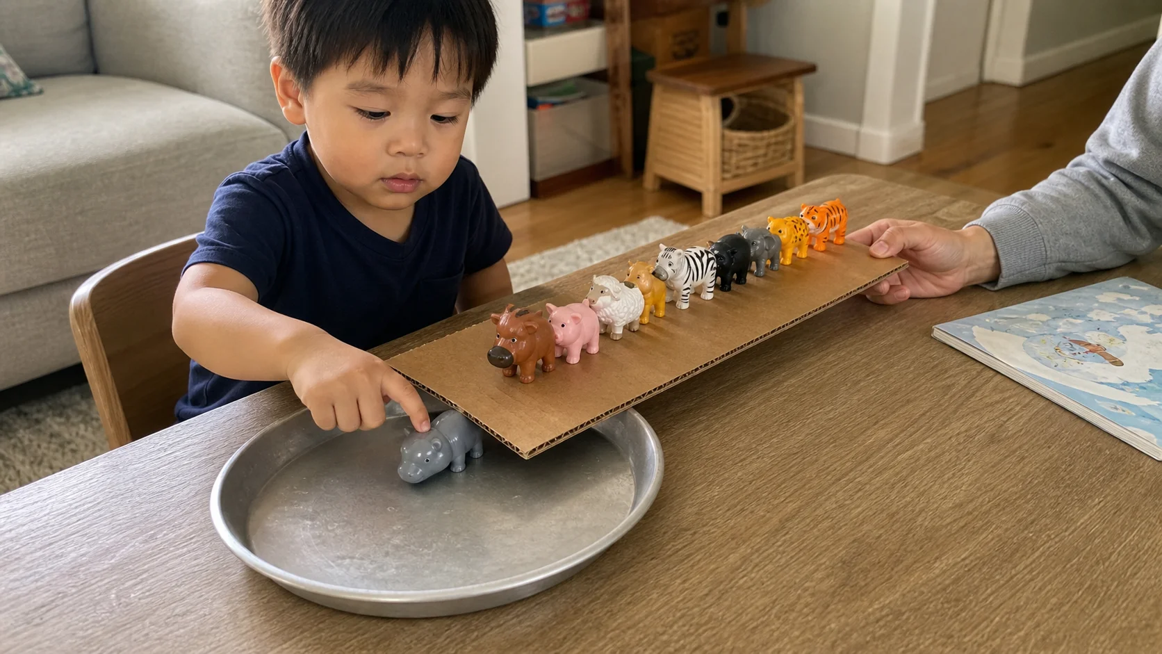 A child knocks one toy animal from a flat board into a metal tray while a grown-up steadies the board nearby.