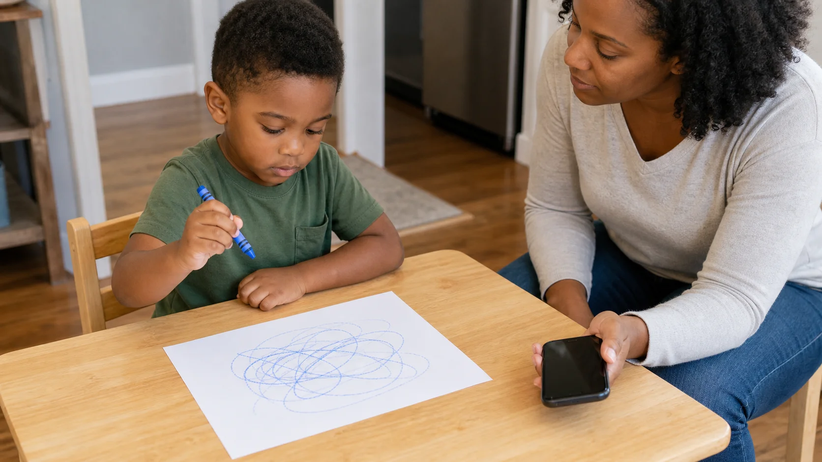 A child drawing on one sheet of paper while a grown-up nearby holds a phone ready to pause the music.